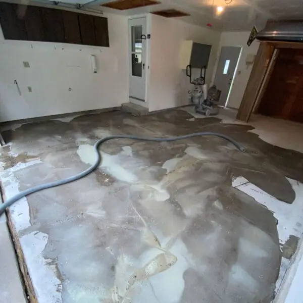 A partially renovated room with an uneven concrete floor, a hose, and a few tools visible. No recognizable landmarks present.