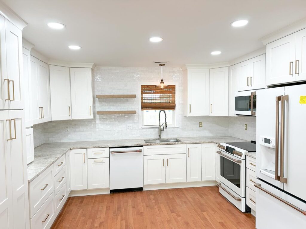 Bright, modern kitchen with white cabinets, granite countertops, and stainless appliances. Wooden floor complements sleek design. Window with blinds above the sink.