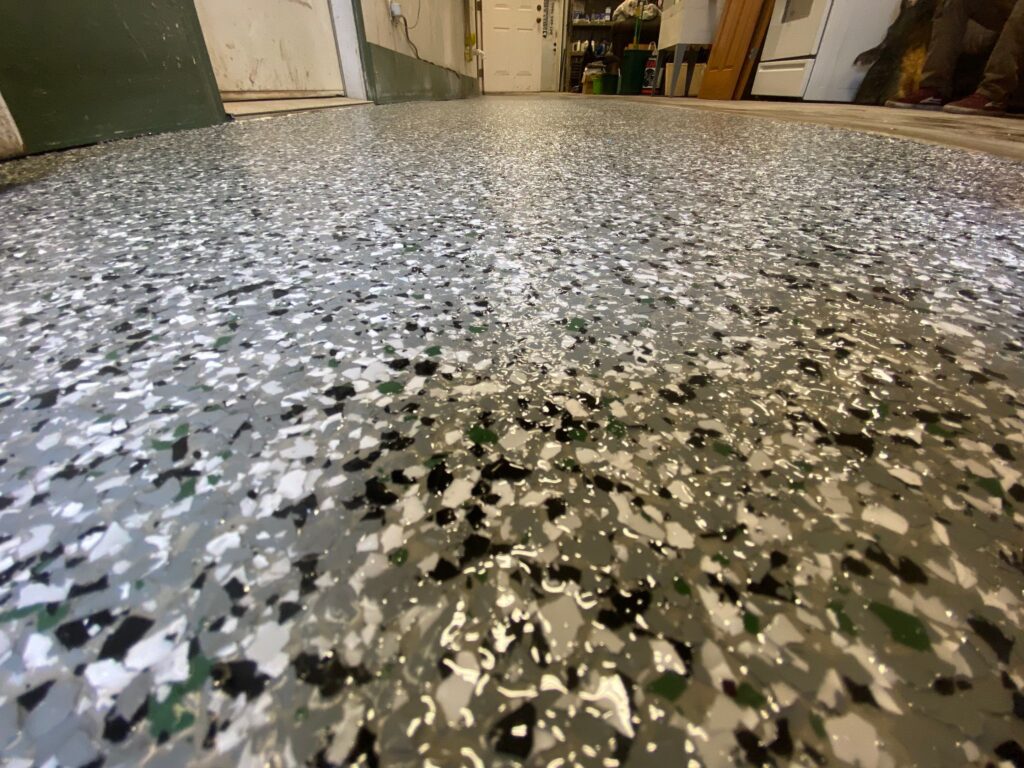 Close-up view of a speckled epoxy floor with various color chips in a room, showcasing smooth, shiny finish, and wall background.