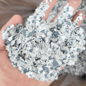A person holds a handful of small, shredded, white and gray plastic pieces, creating a textured and fragmented appearance against a blurred backdrop.